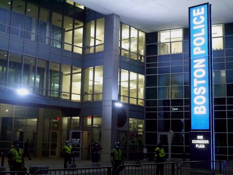 Entryway to Boston Police headquarters taken at night with officers in riot gear standing outside.
