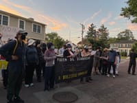Protesters standing on the street in front of Governor Healey's home hold a sign reading "Stop terrorizing our families" in Spanish.