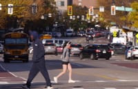 A Black man heads south west in the pedestrian crossing at Washington and Lenox streets while an Asian woman jogs in a northeast direction.
