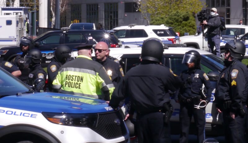 Boston police officers gather at the site of a Northeastern University student protest against Israel's siege of Gaza while a camera operator looms in background.